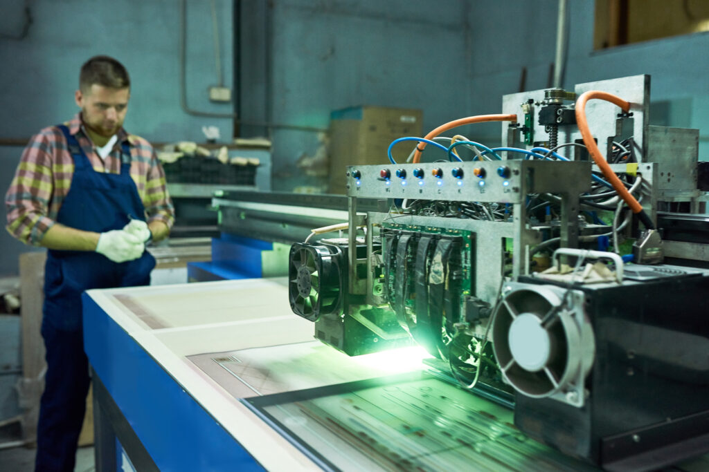 Modern laser engraving equipment in industrial workshop, machine processing glass with unrecognizable operator in background, copy space